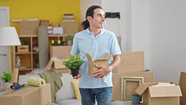 Orta yaşlı bir adam yeni evinde kendine güvenen bir paket ve bitki tutuyor. - Video, Çekim