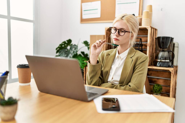 Mujer joven rubia trabajadora de negocios usando portátil pensando en la oficina - Foto, Imagen