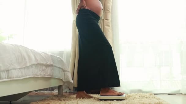 Zorgen voor de gezondheid van zwangere vrouwen en nieuwe moeders: Zwarte Afro-Amerikaanse zwangere vrouw loopt op grote schaal om gewicht te meten zorgt voor haar gezondheidsbalans haar eigen lichaam in de slaapkamer. - Video