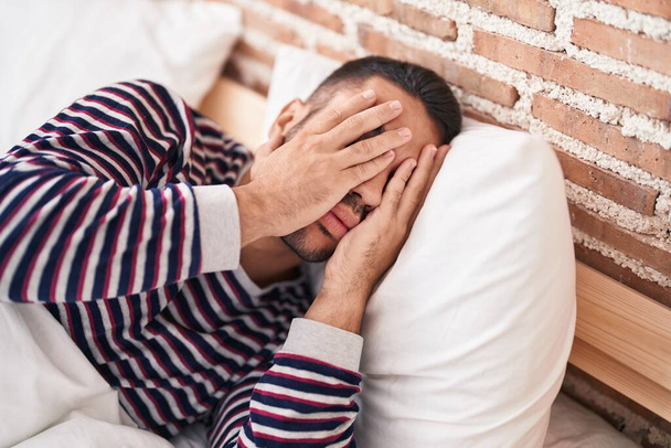 Young hispanic man stressed lying on bed at bedroom - Foto, immagini