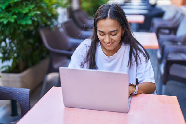 Mladá krásná hispánská žena pomocí notebooku sedí na stole na terase kavárny - Fotografie, Obrázek