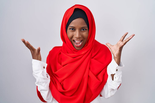 Junge arabische Frau mit traditionellem islamischen Hijab-Schal feiert verrückt und erstaunt über den Erfolg mit erhobenen Armen und offenen Augen, die aufgeregt schreien. Siegerkonzept  - Foto, Bild