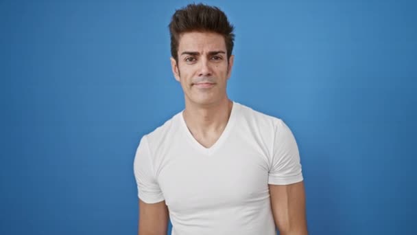 jonge Spaanse man glimlachend zelfverzekerd wijzend met vingers naar de camera over geïsoleerde blauwe achtergrond - Video