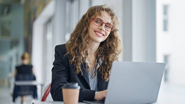 Νεαρή γυναίκα επιχειρηματίας χρησιμοποιώντας φορητό υπολογιστή χαμογελώντας στο γραφείο - Φωτογραφία, εικόνα