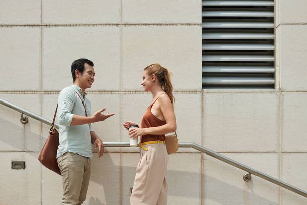Sorridente giovane asiatico uomo chiedendo fuori giovane donna quando che sono in piedi su passi all'aperto - Foto, immagini