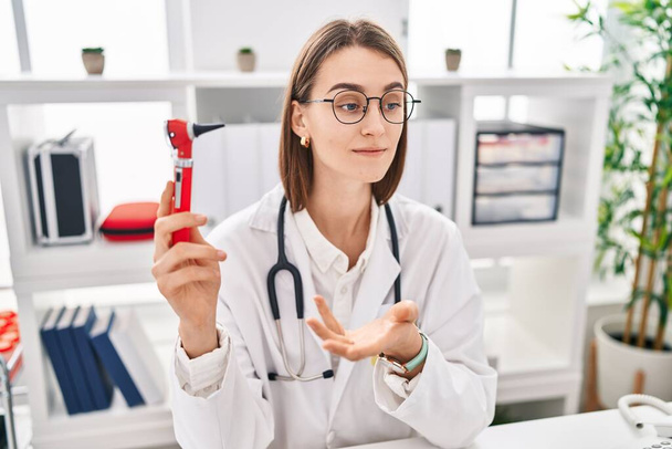 Mujer joven caucásica médico sosteniendo otoscopio en la clínica - Foto, Imagen