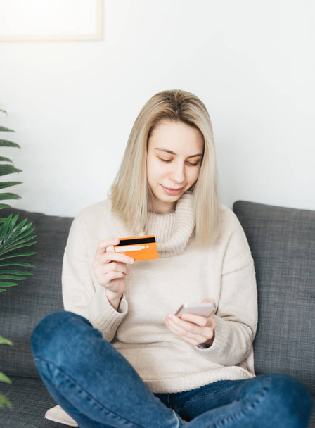 Mladá žena držící smartphone a bankovní kreditní kartu, zapojená do online mobilního nakupování doma, šťastná žena nakupující zboží nebo služby v internetovém obchodě. - Fotografie, Obrázek