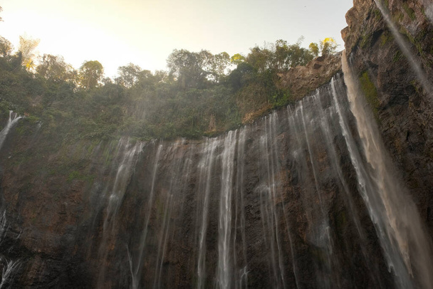 Kijk omhoog in ontzag naar de majestueuze Tumpak Sewu Waterval, staand hoog en krachtig. De brullende waterval creëert een betoverend spektakel, dat de essentie van de grandeur van de natuur vastlegt. - Foto, afbeelding