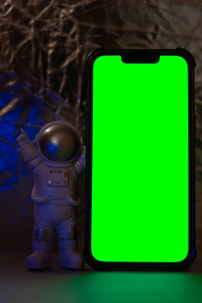 Plastic toy figure astronaut with mobile phone chroma key green screen for your advertisement Copy space. Concept of out of earth travel, private spaceman commercial flights. Space missions and - Photo, image