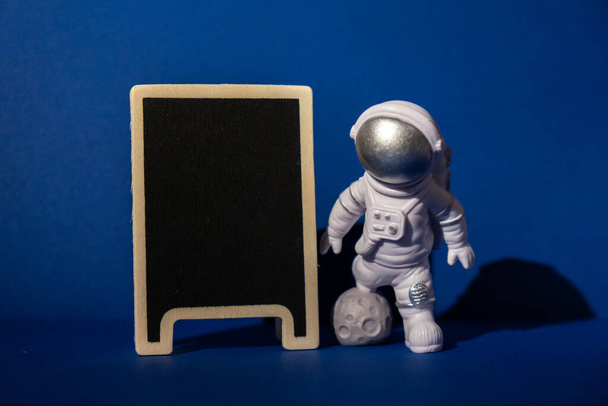 astronauta giocattolo di plastica con modello lavagna modello per il vostro testo su sfondo blu colorato Copia spazio. Concetto di viaggi fuori terra, voli commerciali spaziali privati. Missioni spaziali e - Foto, immagini