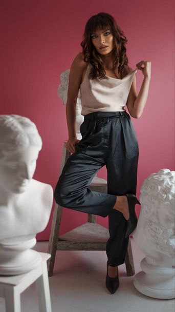 Stunning brunette set against Grecian art on a rosy studio canvas. Where elegance meets history - Photo, Image
