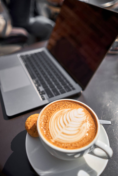 Eine Tasse Capuchino-Kaffee. Der Tisch im Coworking Space des Coffeeshops. Eine Tasse Kaffee auf der Veranda an einem sonnigen Tag. Kaffeepause im Café. Nahaufnahme. Hochwertiges Foto. - Foto, Bild