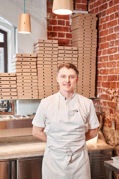 De chef bereidt pizza in een Napolitaanse pizzeria. Kook in een schort in de keuken met een schop in zijn handen. dozen voor voedsellevering op de achtergrond. Hoge kwaliteit foto - Foto, afbeelding