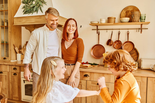 joyful parents looking at excited kids playing and having fun in kitchen, siblings relationship - Photo, Image