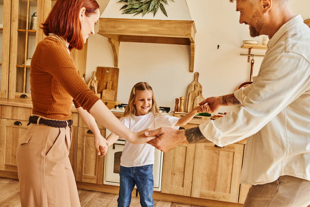 cheerful parents with adorable daughter holding hands and playing in kitchen, fun and laughter - Photo, Image