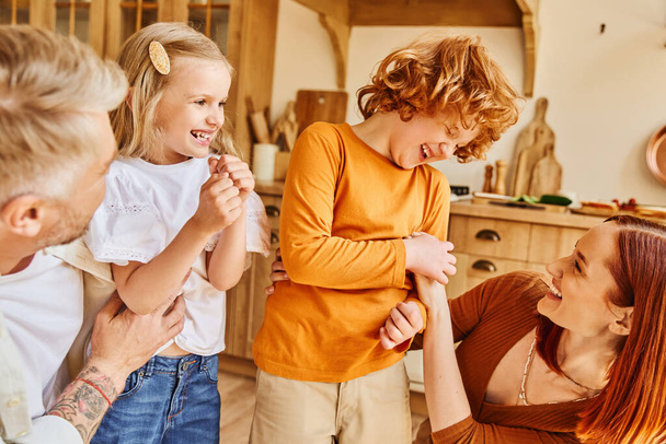onnellinen vanhemmat kutittavat innoissaan lapsia ja hauskaa modernissa keittiössä kotona, liimaus hetkiä - Valokuva, kuva