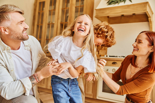 szerető szülők csiklandozza izgatott gyerekek modern konyha, szórakozás és nevetés hangulatos otthoni környezetben - Fotó, kép