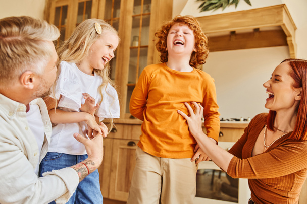 Glückliche Eltern kitzeln überglückliche Kinder in der modernen Küche, Spaß und Lachen in gemütlicher häuslicher Umgebung - Foto, Bild