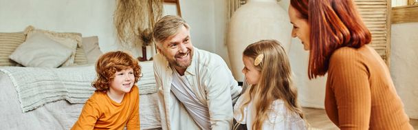 радісні батьки з дочкою і сином дивляться один на одного у вітальні вдома, горизонтальний банер - Фото, зображення