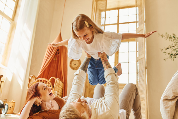 mulher rindo olhando para o marido brincando com a filha no chão na sala de estar, momentos de ligação - Foto, Imagem