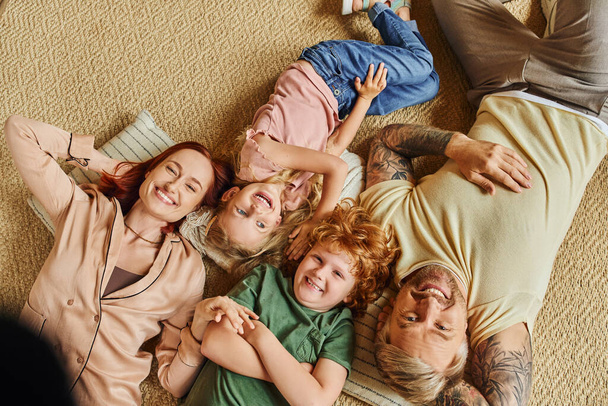 top view of smiling parents and children lying down on floor in living room and smiling at camera - Photo, Image