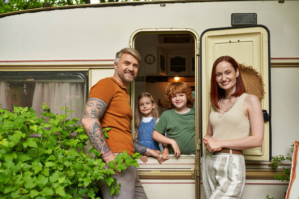 smiling parents looking at camera near happy children in trailer home, family leisure and recreation - 写真・画像