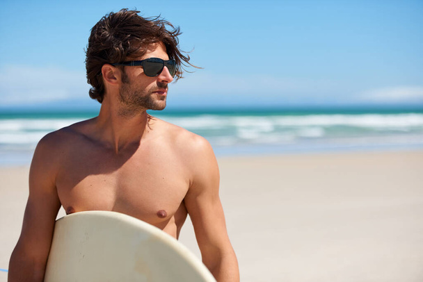 Man tinkelen, surfen en reizen met een zonnebril aan het strand en de zee voor fitness en watersport met mockup ruimte. Vertrouwen, mannelijk persoon en surfplank voor training en training door de oceaan met vrijheid. - Foto, afbeelding