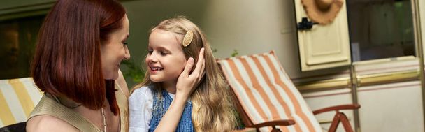 joyeuse femme caressant les cheveux de fille adorable tout en étant assis à côté de la maison de remorque, bannière - Photo, image