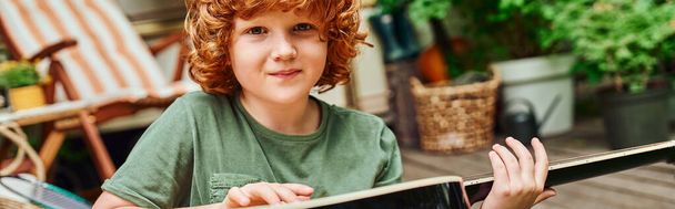 redhead kid with acoustic guitar looking at camera while sitting near modern trailer home, banner - Photo, Image