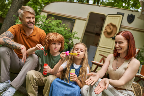 近代的なトレーラーの家の隣の幸せな両親の近くで石鹸の泡を吹くかわいい子供,余暇および楽しみ - 写真・画像