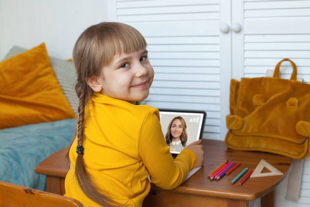 Милый маленький ребенок улыбается во время учебы в Интернете и разговаривает с учителем - Фото, изображение