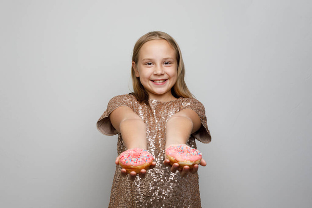 Прекрасна дівчинка показує солодкі рожеві пончики на сірому фоні - Фото, зображення