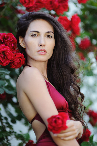 Portrait of beautiful brunette girl in red roses - Φωτογραφία, εικόνα