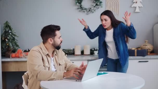 Zdenerwowana wściekła żona zwraca się do męża pochłoniętego laptopem podczas świąt Bożego Narodzenia w kuchni, przedstawiając finansowe napięcia powodujące rodzinne spory. Kameralna kłótnia domowa podczas Nowego Roku - Materiał filmowy, wideo