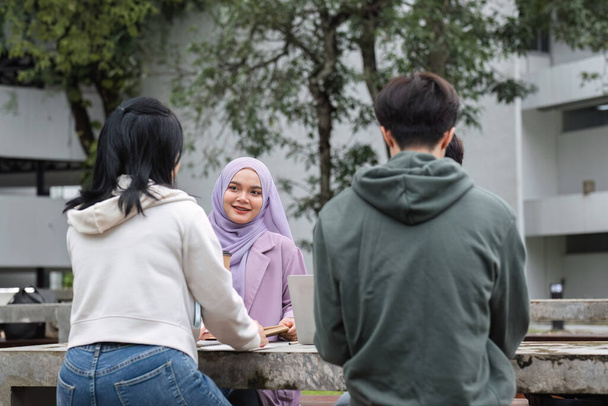 Un gruppo multirazziale di studenti del college, compresi gli studenti musulmani e asiatici, sedeva su panchine in una zona di pausa campus. Leggere libri o studiare insieme per gli esami.. - Foto, immagini