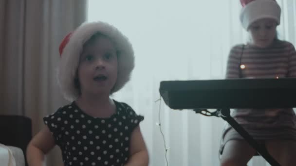 Bambine che danno una festa di Natale a casa. Alle sorelle piace cantare canzoni natalizie insieme e ballare a casa. Atmosfera gioiosa. Riflesso anamorfico della lente - Filmati, video