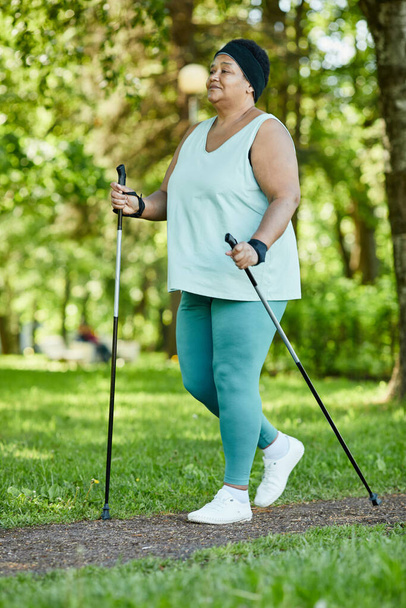 Portret dojrzałej czarnej kobiety spacerującej z kijkami w parku podczas treningu na świeżym powietrzu - Zdjęcie, obraz