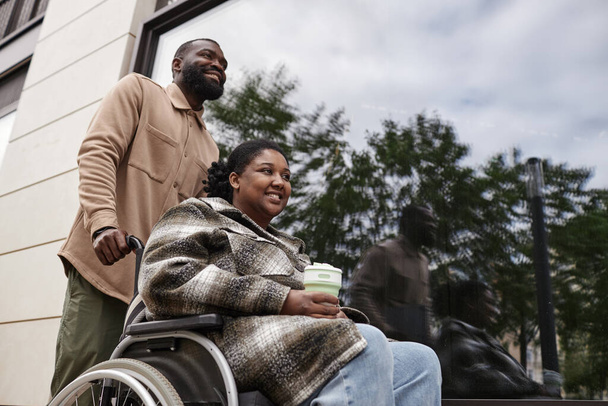 Tiefer Winkel Porträt eines lächelnden schwarzen Paares mit Partner im Rollstuhl im Freien in der Stadt Einstellung - Foto, Bild