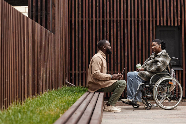 Foto grafica laterale di una giovane donna sulla sedia a rotelle che parla con un amico o un collega all'aperto nel parco cittadino, copia lo spazio - Foto, immagini