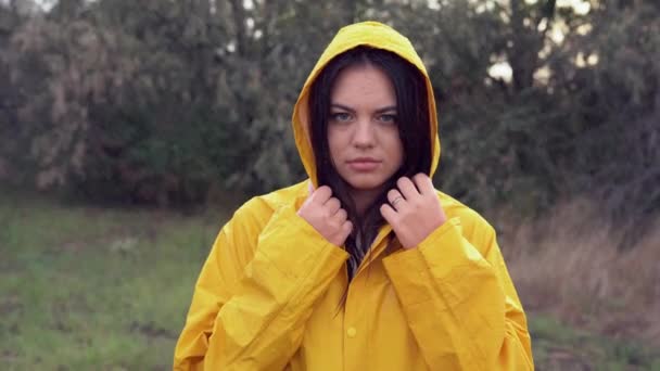 close-up retrato de uma jovem mulher bonita em uma capa de chuva amarela durante a chuva com um rosto insatisfeito e emoções negativas, de pé olhando para a câmera e suspirando pesadamente. - Filmagem, Vídeo