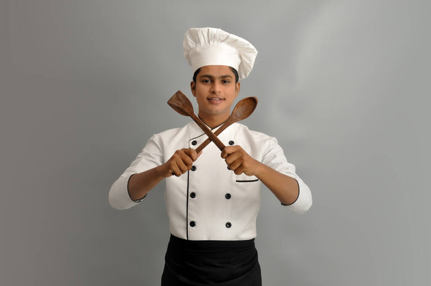 Ευτυχισμένος αρσενικός σεφ ντυμένος με στολή κρατώντας ξύλινη κουτάλα και πλάστη - Φωτογραφία, εικόνα