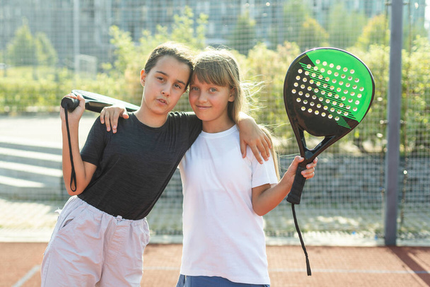 Teenage girls with racquets and balls standing in padel court, looking at camera and smiling. High quality photo - Photo, Image