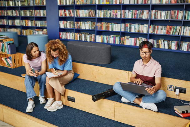 Levendige full length shot van diverse groep studenten in de universiteitsbibliotheek doen huiswerk, kopiëren ruimte - Foto, afbeelding