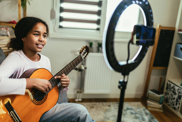 Young teenager playing guitar and recording vlog and music tutorial for the Internet. - Foto, immagini