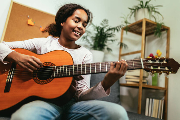 African american teenage girl sitting on couch in her room and learning to play guitar - Foto, immagini