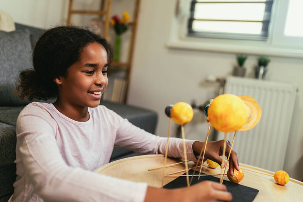 Happy african american school girl making a solar system for a school science project at home - Fotó, kép