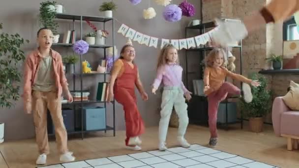 Komplette Aufnahme einer Gruppe multiethnischer Kinder, die lustige körperliche Übungen durchführen, während sie von einem anonymen Off-Schauspieler im Charakterkostüm auf einer privaten Geburtstagsparty unterhalten werden - Filmmaterial, Video