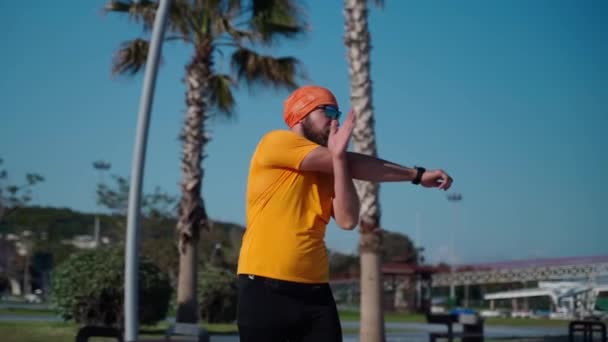 Körperpositiver Mann in Sportbekleidung macht Aufwärmen von Muskeln und Gelenken vor dem Lauftraining Vorbereitung auf den Jogging-Marathon sonniger Tag Laufband Handfläche Hintergrund - Filmmaterial, Video