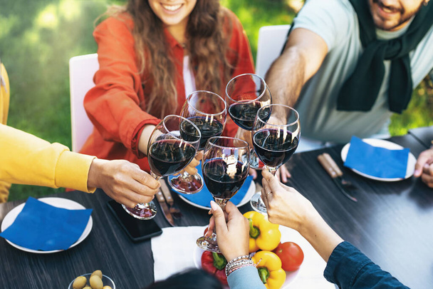 Yksityiskohta viinilaseista juomassa maljaa sisäpihan pöydällä. Nuorten ystävien epäselvät kasvot vihjaavat iloiseen kokoontumiseen.. - Valokuva, kuva