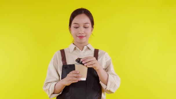 Portrait of young asian barista woman wearing apron smell coffee cup on yellow background, waitress or entrepreneur holding coffee with excited, small business or startup, waiter of cafe. - Footage, Video